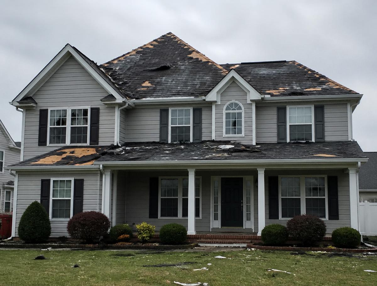 Two-story home with storm-damaged roof and torn shingles